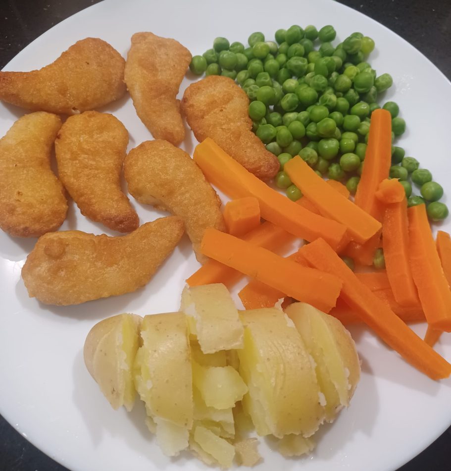 Plate of chicken nuggets, green peas, carrot sticks, and mashed potatoes.