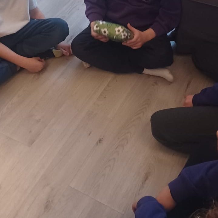 Children sitting on the floor, holding and passing around a wrapped gift.