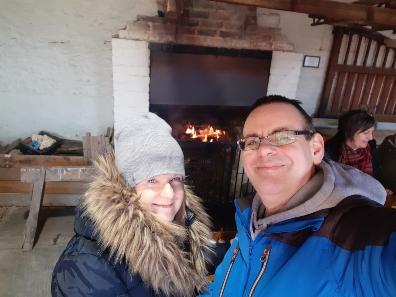 A man and a woman smiling together indoors near a fireplace.