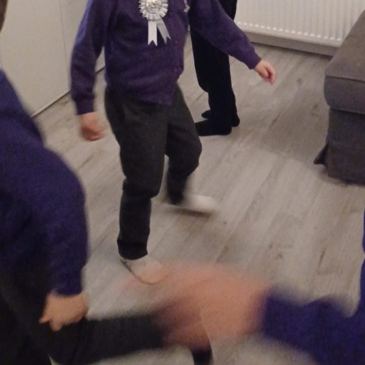 Two children in purple sweaters dancing on a wooden floor.