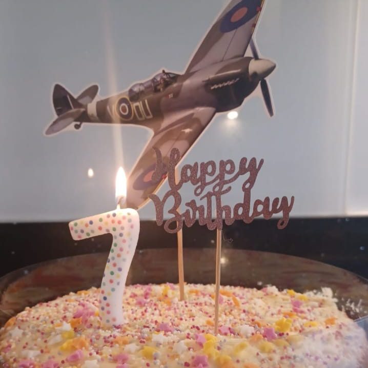 Birthday cake with a Spitfire plane topper and a "Happy Birthday" sign, celebrating 7 years.
