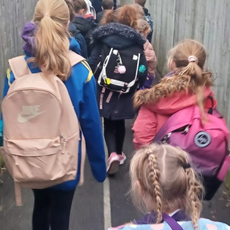 A group of children walking along a path, each carrying backpacks.